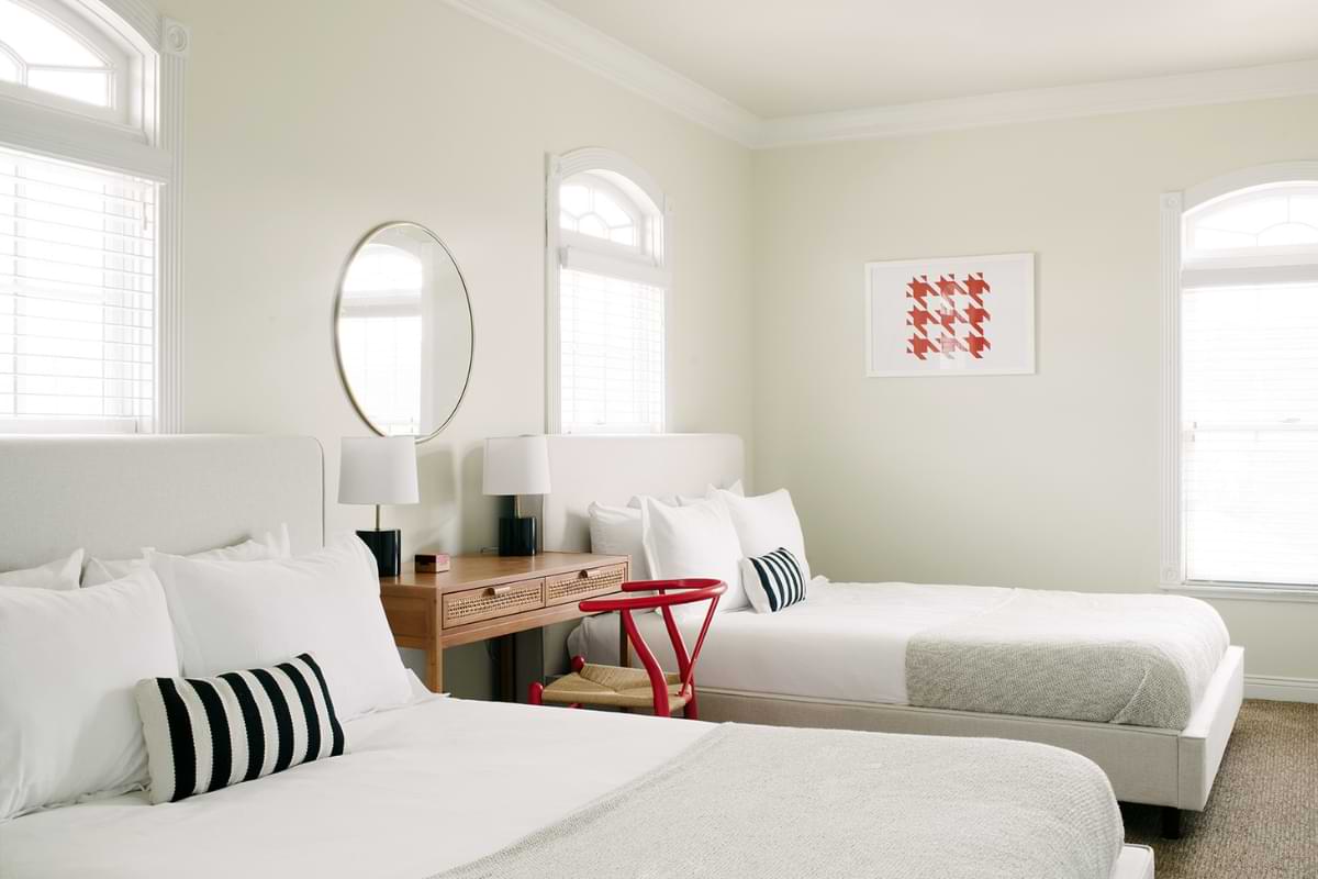 A well-lit and white room show two queen-sized beds with a desk separating them. 