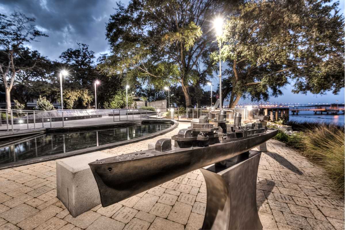 A statue of a naval ship sits in an open-air memorial site on the waterfront. 