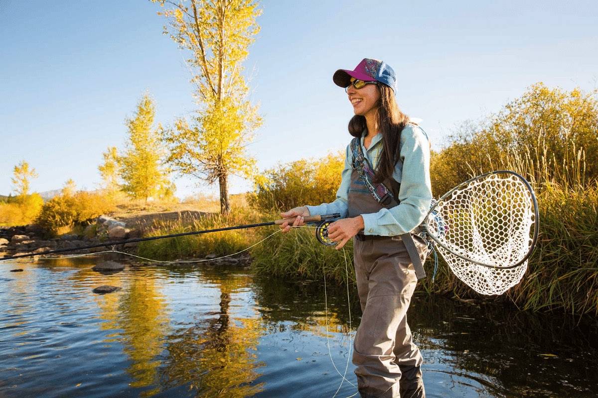 A woman stands in a body of water holding a fly fishing net with a casted fishing line in front of her