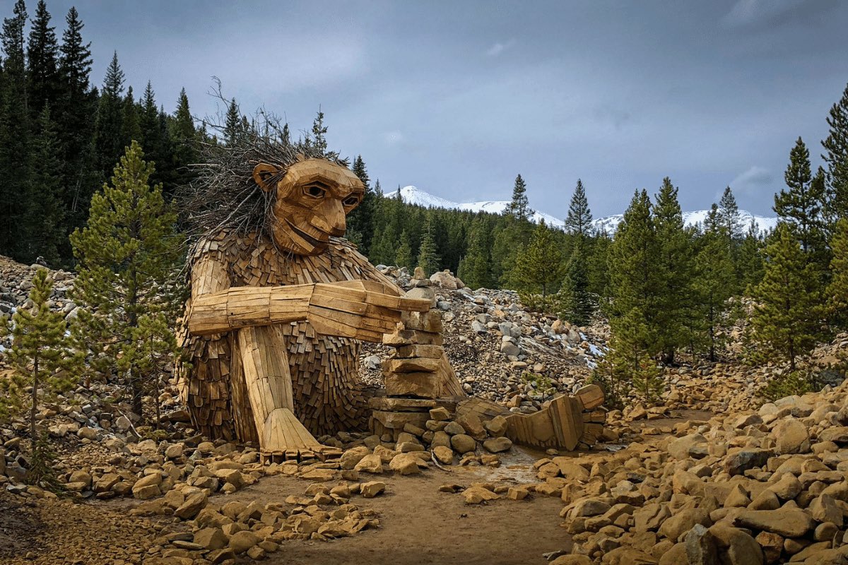 The wooden mascot of Breckenridge, Isak Heartstone, sits surrounded by tall pine trees and discount snowy mountains