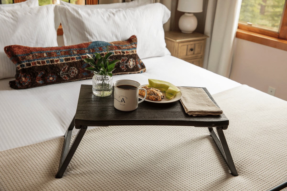An AvantStay mug with tea sits atop a bedroom tray next to a plate with a scone and some fruit