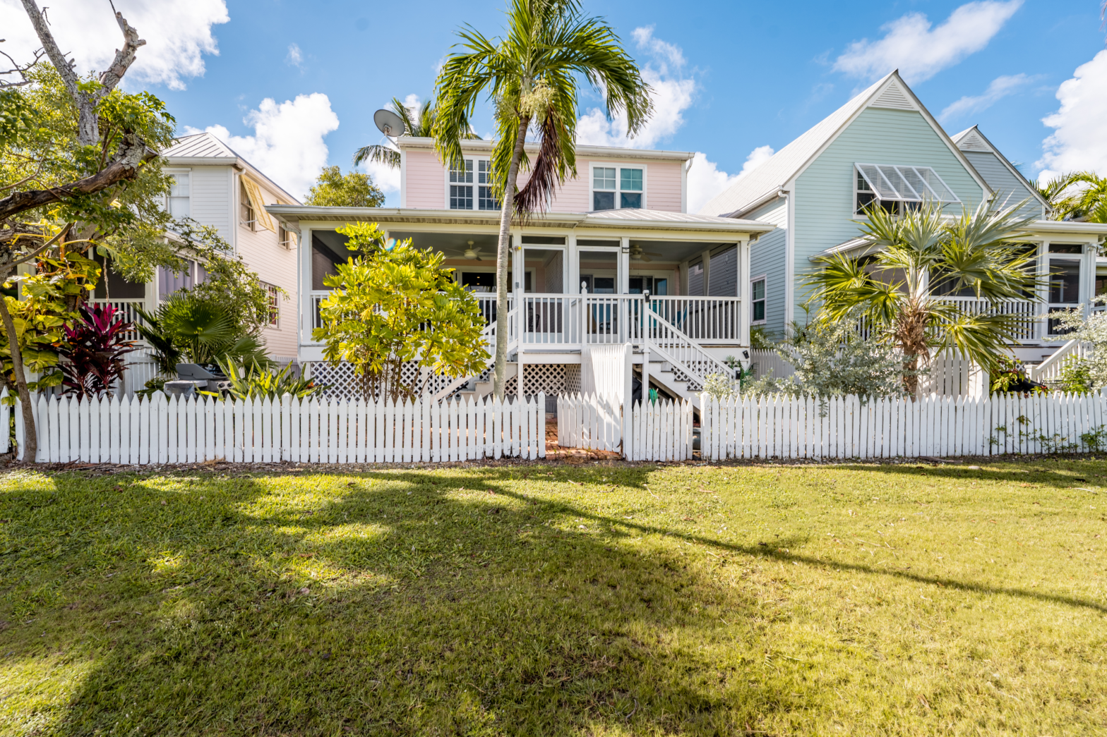 green backyard and palm trees of a beach house with white picket fence
