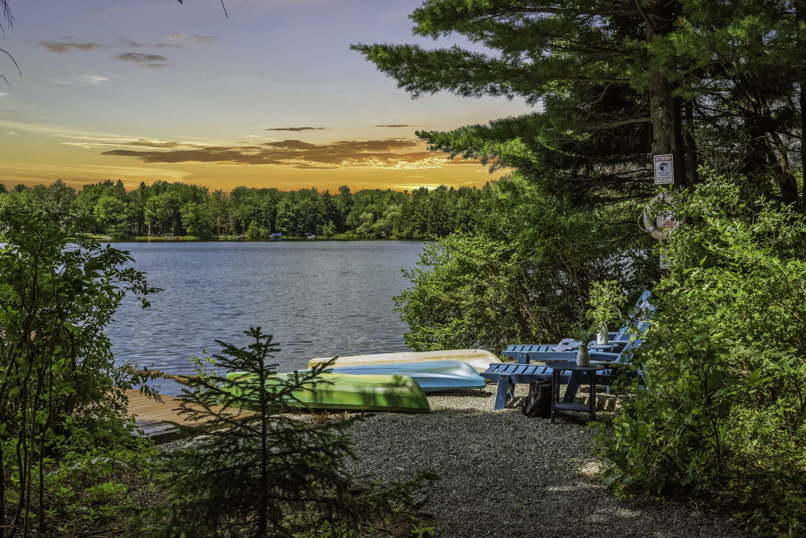 hidden dock in the green lush pine trees with 3 green and blue canoes under the sunset orange sky