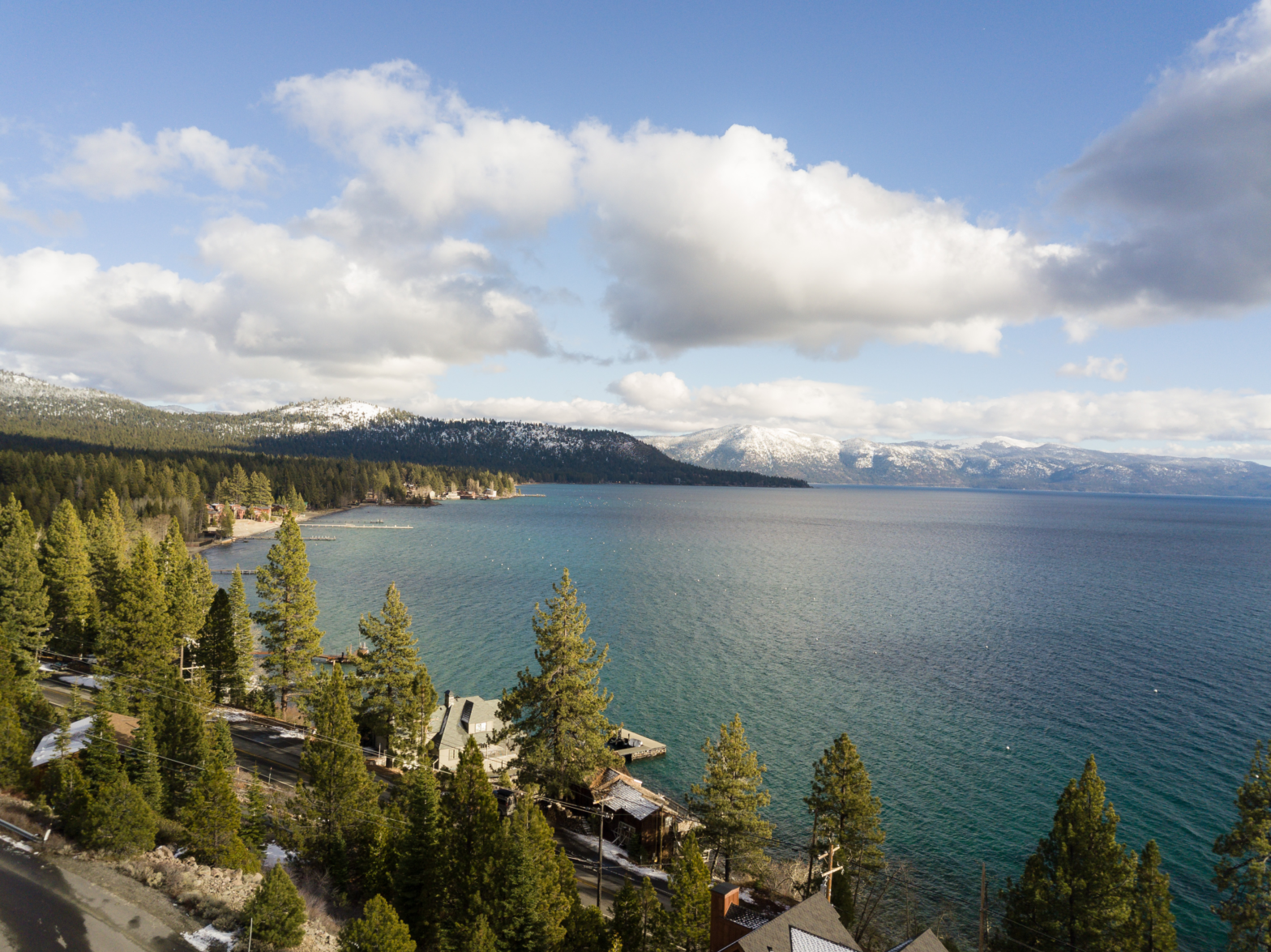 overview shot of the big blue lake surrounded by dark green pine trees and reflecting the cloudy skies