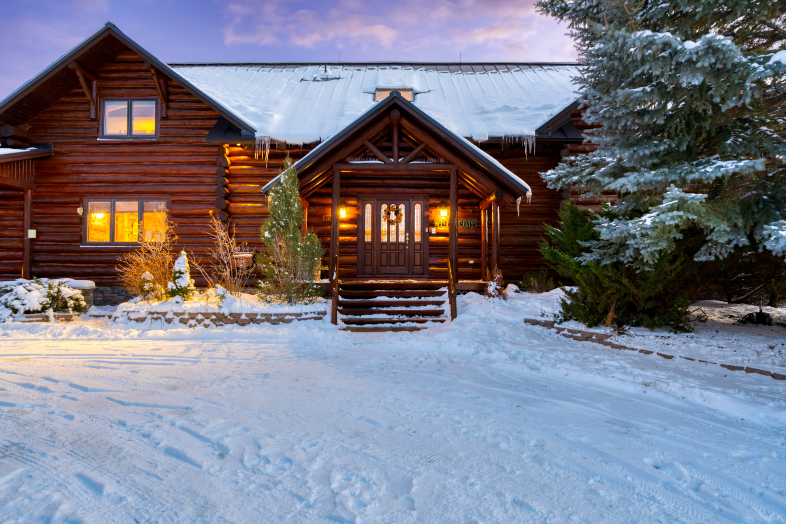 brown log cabin burried in snow with pine trees and warm lights